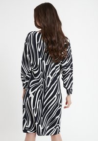 Robe noire et blanche, longueur genoux, avec un motif ondulé abstrait, manches bouffantes longues et coupe décontractée. Tissu lisse avec des détails minimaux.