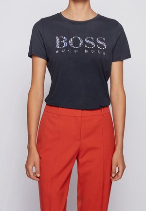Dark gray short-sleeve t-shirt with "BOSS" logo in a patterned design. Paired with bright red tailored pants. Simple crew neck.