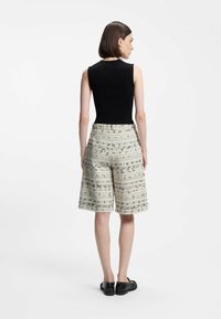 Haut noir sans manches associé à un short beige à motifs avec des rayures texturées, et des chaussures noires fermées. Design simple et moderne.
