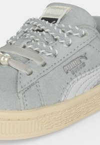 Ανοιχτό γκρι sneaker Puma Suede με υφή μπεζ σόλας, πλεκτά και επίπεδα κορδόνια, και το λογότυπο Puma στο πλάι και στη γλώσσα.
