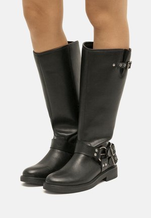 Bottes noires montantes en cuir synthétique, dotées d'une sangle avec une boucle en argent et d'une semelle en caoutchouc plate pour la stabilité.