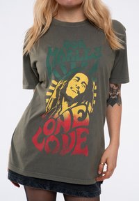 Olive green cotton T-shirt featuring a printed graphic of Bob Marley with red, yellow, and green text stating "One Love" and sun rays design.