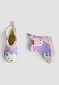 Bottes en caoutchouc violettes avec un intérieur doux beige. Elles présentent un visage de chat blanc sur le bout avec un accent floral et un talon rose. Fond avec un motif d'étoiles.