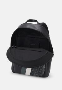 Zaino nero con apertura zip, materiale tessile, loghi a contrasto, texture liscia e tasca frontale con chiusura a patta.