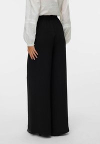 Pantalons noirs à jambes larges avec une coupe décontractée et une taille élastique, associés à une chemise blanche à manches longues avec des accents texturés.