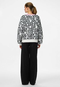 Przesadny sweter w czerni i bieli z dużymi wzorami tekstowymi. Przytulny materiał z prążkowanymi mankietami i okrągłym dekoltem. Połączony z szerokimi czarnymi spodniami.