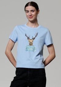 T-shirt en coton bleu clair avec un motif imprimé d'un cerf portant une chemise rayée. Manches courtes et col rond.