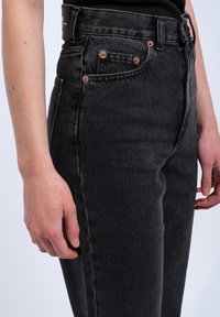 High-waisted black denim jeans with a smooth texture, copper button accents, and classic five-pocket design.