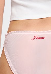 Bragas de malla color rosa claro con un borde festoneado y texto bordado en rojo que dice "Petam." Presentan una textura suave y translúcida para mayor comodidad.