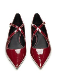 Ballerine in pelle verniciata rossa con punta affusolata, dotate di cinturini incrociati e fibbie metalliche, caratterizzate da una superficie liscia e un interno nero.