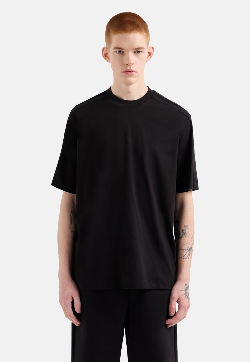 T-shirt nera a maniche corte realizzata in tessuto morbido, con scollo rotondo e sottili accentuazioni testurizzate sulle spalle.