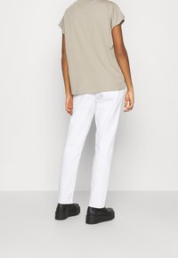 Beige oversized T-shirt met korte mouwen, gecombineerd met witte slim-fit broek en zwarte schoenen. Glad materiaal; minimalistisch ontwerp.