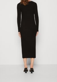 Robe longue noire à manches longues côtelées avec une silhouette moulante et une longueur midi, dotée d'un ourlet festonné et d'un col rond.