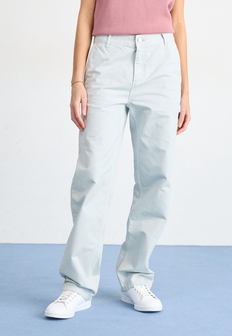 Light blue cotton trousers with a relaxed fit, featuring a front button closure and side pockets, paired with white sneakers.