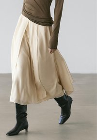 Beige luchtige rok met een gelaagd ontwerp, gecombineerd met zwarte, kniehoge, spits toelopende laarzen. De top heeft lange mouwen en is bruin, met een aansluitend silhouet.