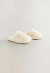 Bežinės, pūkuotos šlepetės su apvalia forma ir švelniu tekstūros paviršiumi. Su plokščiu padu ir atviru užpakaliu, kad būtų lengva dėvėti.