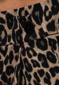 Ύφασμα με μοτίβο λεοπάρδαλης και μαύρο κουμπί σε ένδυμα με ψηλή μέση, παρουσιάζοντας λεπτομέρειες υφής και σχεδίου.