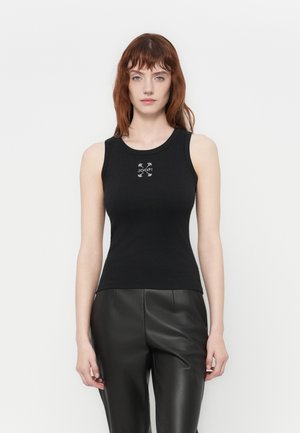 Top nero senza maniche con design aderente, realizzato in un tessuto liscio ed elasticizzato. Presenta un logo al centro. Abbinato a pantaloni in pelle nera.