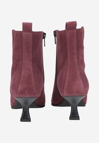 Bottines en suède bordeaux avec un talon effilé, fermeture éclair et une texture lisse. Présente des coutures verticales simples à l'arrière.