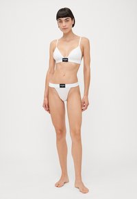 Set di bikini bianco composto da un reggiseno triangolare e un perizoma a vita bassa. Tessuto morbido con dettagli del logo nero sulla fascia. Texture liscia.