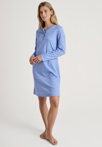 Abito da loungewear azzurro chiaro con maniche lunghe, una fila di bottoni e un motivo a cuori bianchi. Le fessure laterali migliorano il comfort e il movimento.