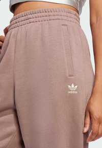 Svijetlosmeđi, opušteni dukserici s elastičnim pojasom, bočnim džepovima i izvezbom Adidas logotipa na lijevom bedru.