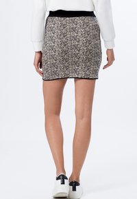 Jupe en tricot à motifs noir et blanc, avec une silhouette ajustée, une taille noire et des détails de couture visibles à l'ourlet.