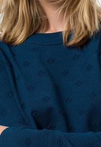 Marineblauwe trui met een gestructureerd patroon van verhoogde kruisen, gemaakt van een zachte stof met een ontspannen pasvorm en een brede halslijn.