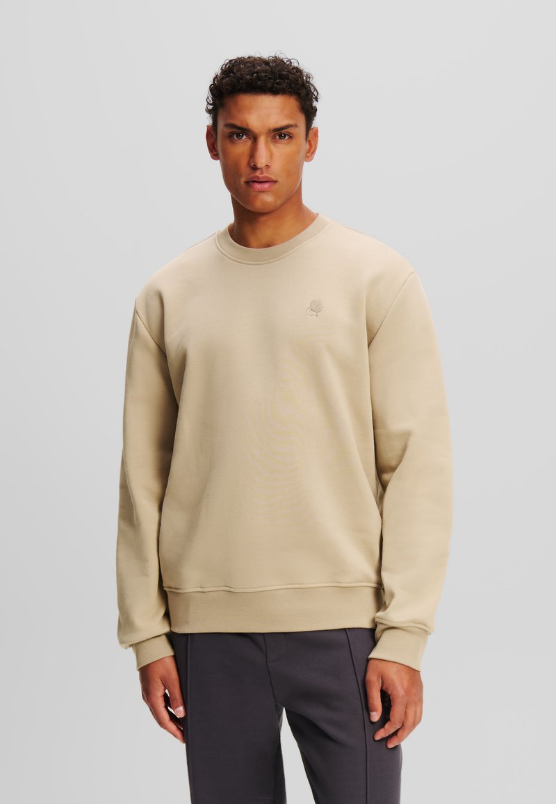 Sudadera beige de cuello redondo hecha de un tejido suave, con puños y dobladillo acanalados, y un pequeño logotipo bordado en el pecho.