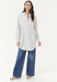 Light blue striped button-up shirt with long sleeves, chest pocket, paired with wide-leg blue denim jeans. Worn with white flip-flops.