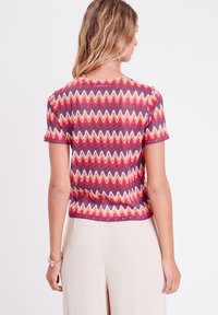 Blouse à manches courtes avec un motif en zigzag en rose, orange, violet et crème. Fabriquée en tissu léger avec un design ajusté et un décolleté arrondi.