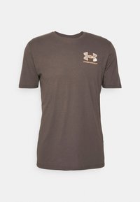 Brun kortärmad T-shirt i bomull, med en orange Under Armour-logga på vänster bröst. Rundad halsringning, klassisk passform.