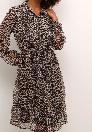 Woman wearing long-sleeve, button-up, knee-length dress with leopard print, one hand on hip and the other touching collar