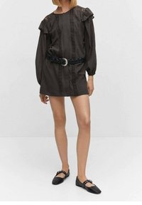 Robe marron foncé avec manches bouffantes, détails en dentelle et motif à rayures centrales. Associée à une ceinture noire tressée et des chaussures plates noires.