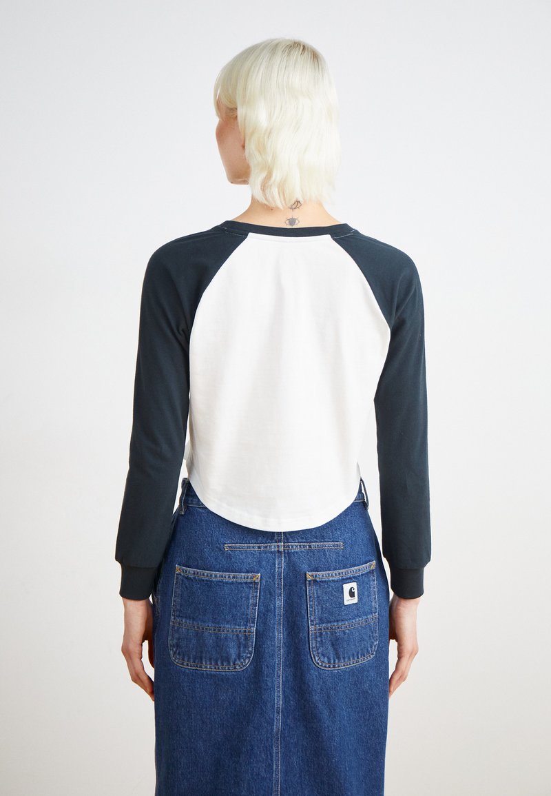 Maglietta a maniche lunghe con maniche raglan blu navy e corpo bianco, con orlo arrotondato. Abbinata a una gonna di jeans con tasche applicate.