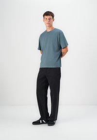 Tricou scurt, gri-albastru, cu mânecă scurtă, asociat cu pantaloni largi negri și adidași negri. Tricoul are un decolteu clasic rotund și o textură moale.