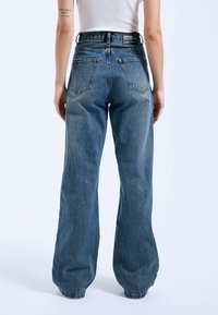 Hoge taille, losse blauwe denim jeans met vijf zakken, zichtbare stiksels en een minimalistisch merkembleem op de achterkant van de tailleband.