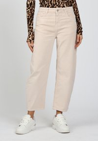 Helle beiger Cordhose mit hohem Bund, geradem Bein und vorderen Taschen, kombiniert mit weißen Sneakers.