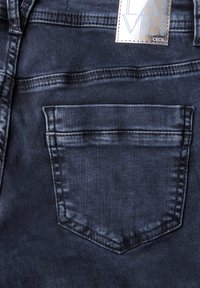 Jeans in denim blu scuro con una tasca posteriore caratterizzata da un bordo cucito dritto. Il tessuto ha una consistenza liscia con sottili variazioni di tonalità.