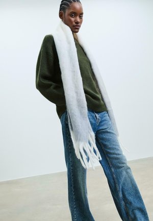Green wool sweater, light gray scarf with fringed ends, and blue denim high-waisted jeans. Smooth texture, casual fit, minimal design.