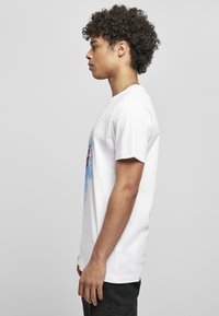 Kortærmet hvid bomulds t-shirt med grafisk print på forsiden, rund halsudskæring og afslappet pasform. Simpelt design med kontrasterende farver.