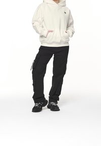 Krämfärgad hoodie med en känguruficka och rosa detaljer, kombinerad med svarta cargo-byxor med flera fickor och svarta sportskor.