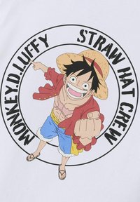 T-shirt arborant un graphique coloré d'un personnage de dessin animé avec des cheveux noirs, un chapeau de paille, une veste rouge et un short bleu dans un design circulaire.