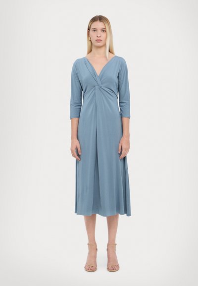 Lichtblauwe jurk tot de knie met een V-hals en driekwart mouwen. Kenmerkt zich door een twistdetail bij de taille en een gladde textuur.