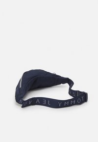 Borsa a tracolla blu navy con una texture morbida, dotata di chiusura con zip e di una tracolla decorata con il motivo "TOMMY JEANS" in grigio chiaro.