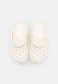 Zoccoli bianchi realizzati in materiale morbido con pois arancioni. Il design include una larga fascia sulla parte superiore e una suola texture.
