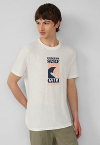 Witte katoenen t-shirt met een grafische print met "ENDLESS SURF", "CALI" en een golvend ontwerp in donkerblauw, koraal en lichtblauw. Korte mouwen, ronde hals.