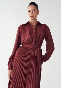 Kastanjapuna pleat-kjole med krage, lange ærmer og en knyttet taljebælte; glat tekstur med knapdetaljer.