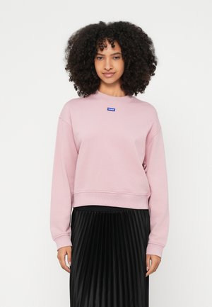Rosa Sweatshirt mit Rundhalsausschnitt aus Baumwollmischung, mit gerippten Bündchen und Saum, kleinem blauem Logo-Patch, kombiniert mit einem schwarzen Faltenrock.
