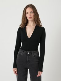 Svart ribbestrikket bodysuit med dyp V-hals, lange ermer og en tettsittende design. Kombinert med høyt liv mørkegrå jeans.